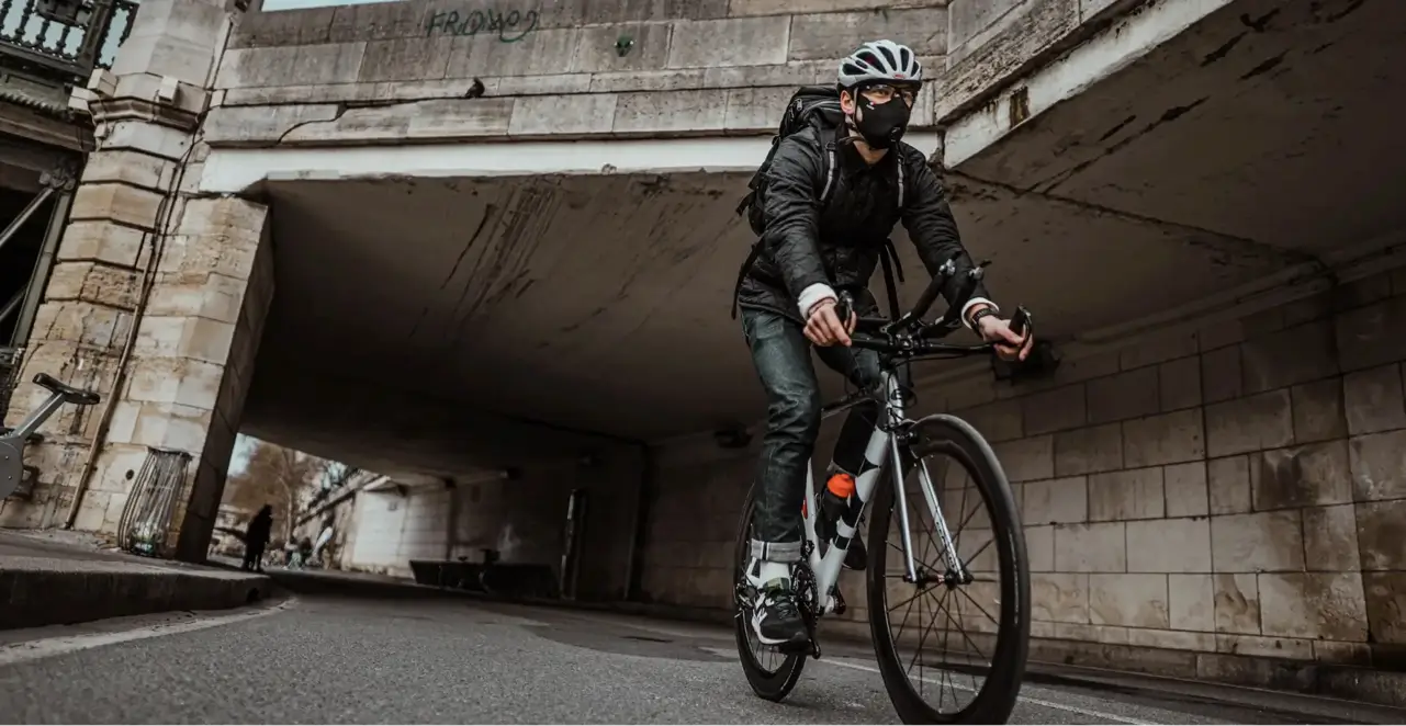 homme sur un vélo qui passe sous un pont avec un masque R-PUR